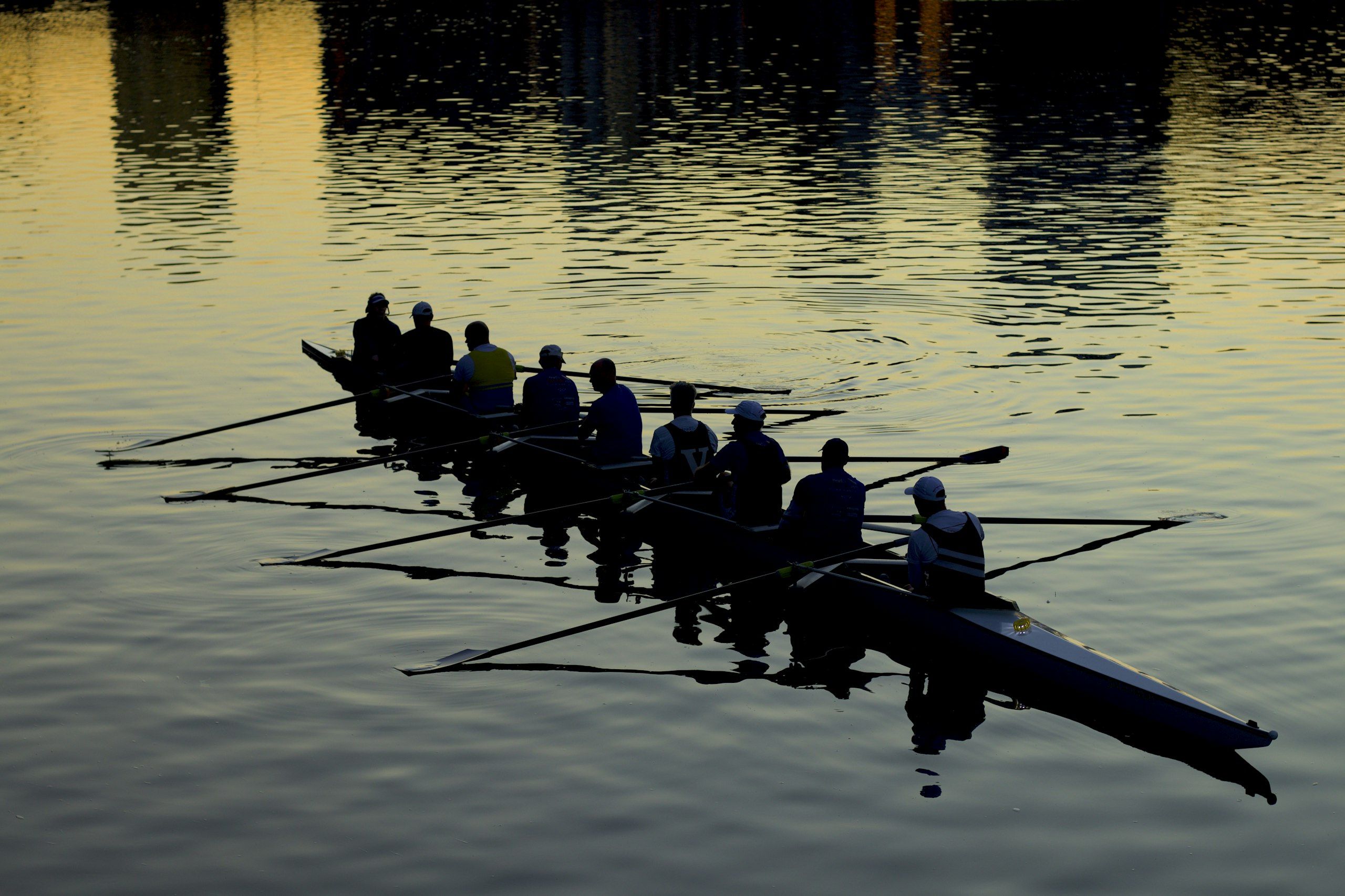 A rowing crew in silhouette pulling in unison on golden water